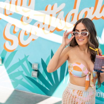 woman at the pool in front of mural with cocktail in hand